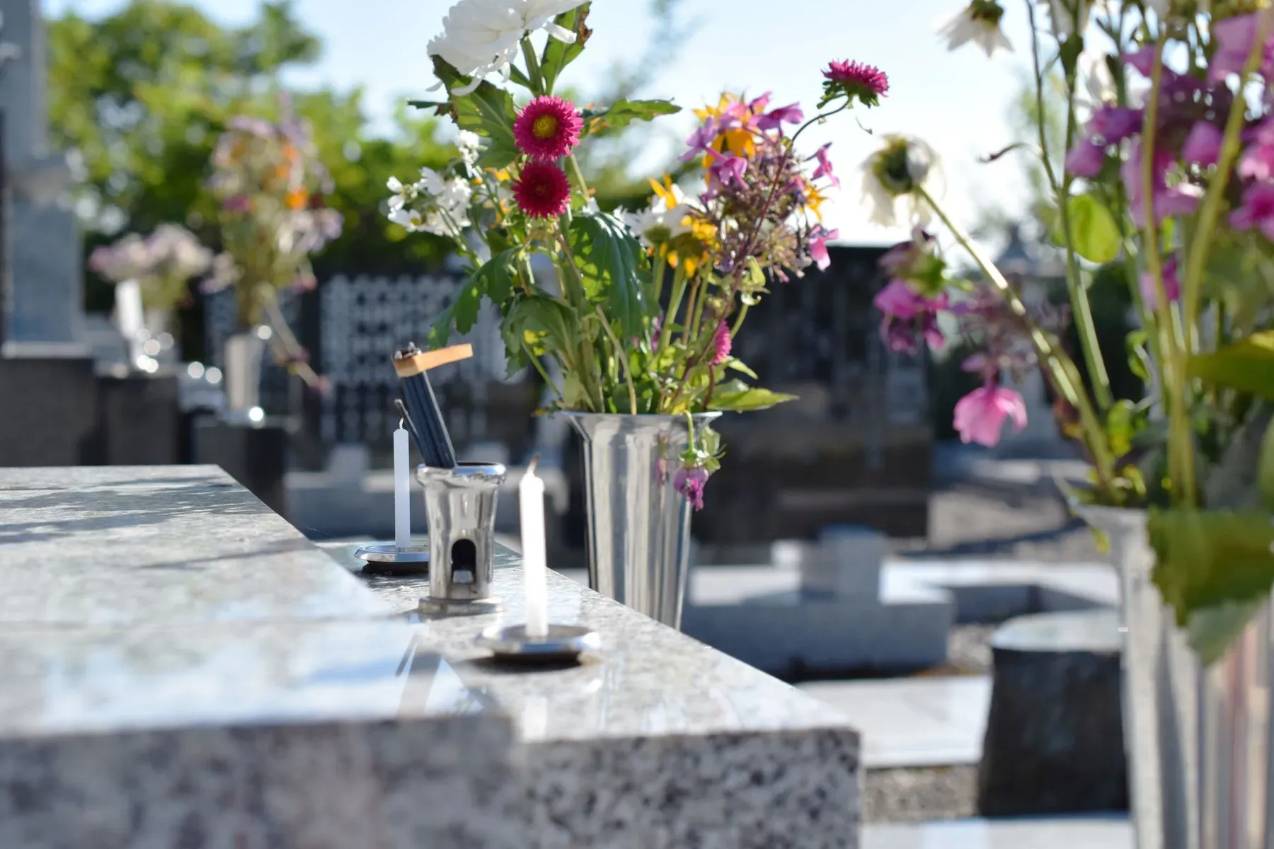 Fleurs de cimetière fraîches et blanches dans des vases sur une tombe en granit.