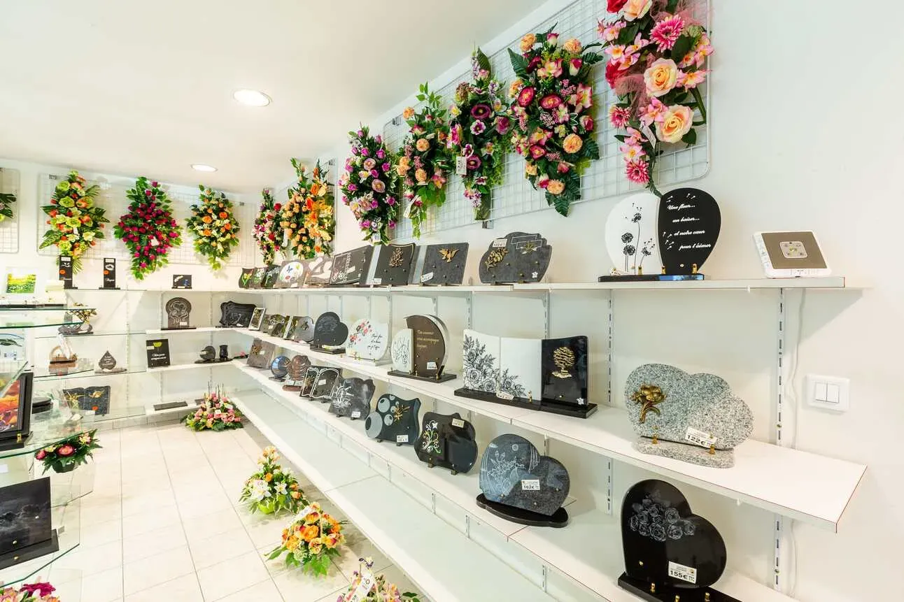 Étagères d'exposition avec plaques funéraires et compositions florales.